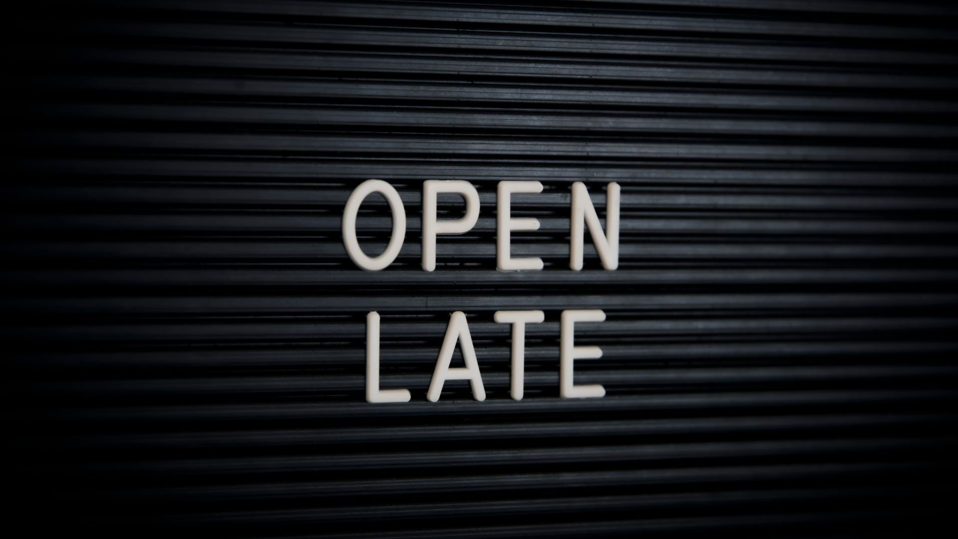 White letters spelling "OPEN LATE" on a dark horizontal striped background